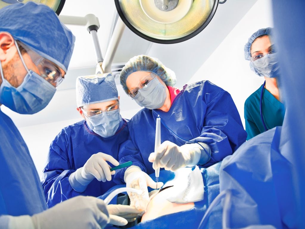 Surgical team in blue gowns and masks performing a procedure under operating room lights